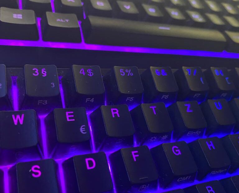 Nahaufnahme einer Computertastatur mit blau und lila leuchtenden Tasten